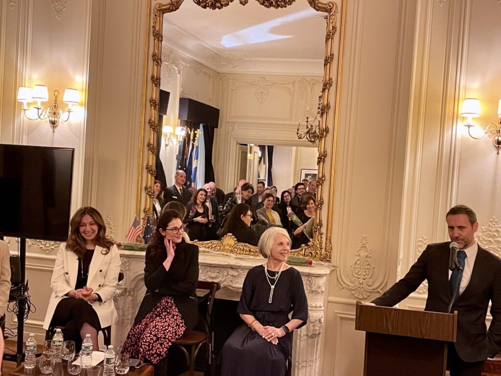 A man at a podium, 3 women sitting