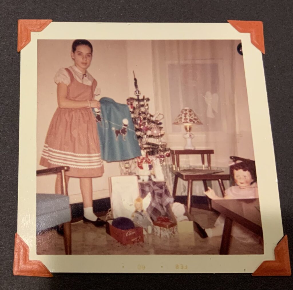 A girl holding a skirt by a Christmas tree with gifts
